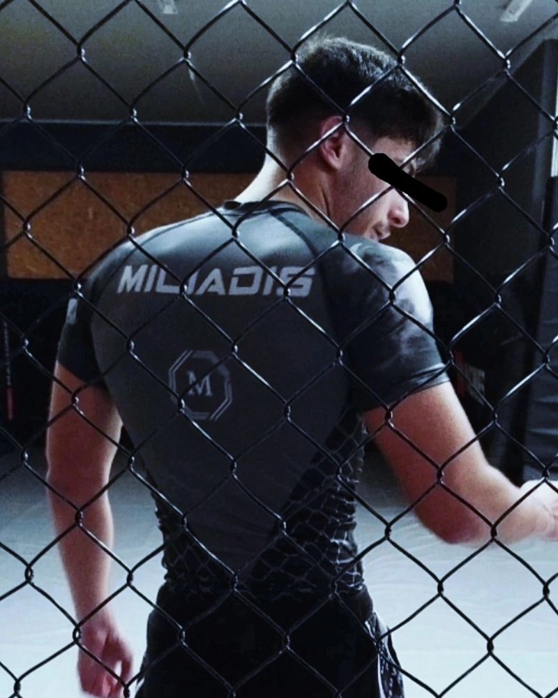 Miliadis Nikos in a fight shirt seen through the cage fence